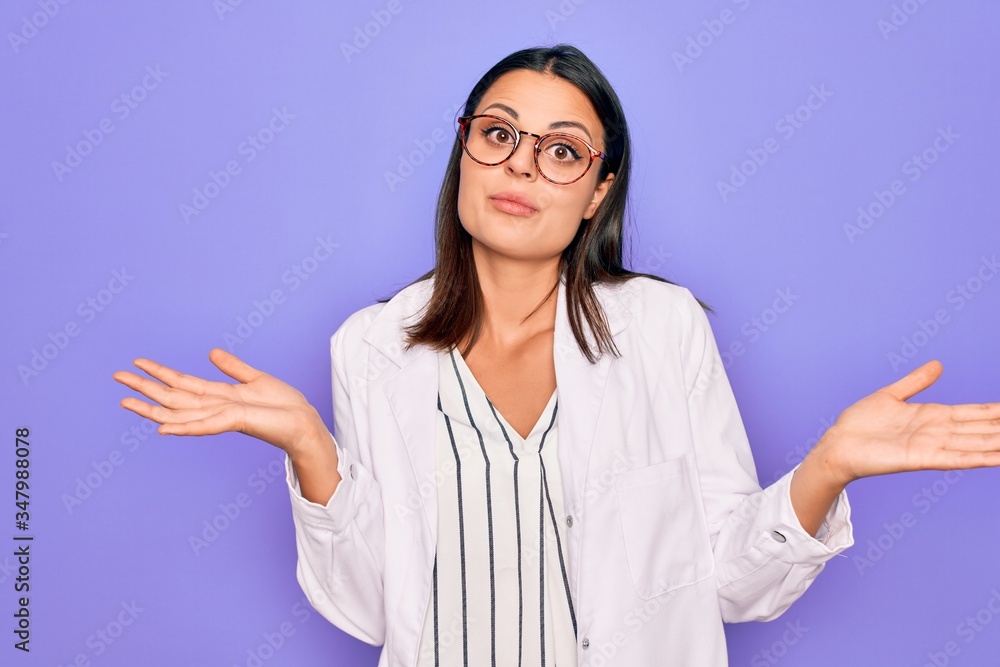 Young beautiful brunette psychologist woman wearing coat and glasses over purple background clueless and confused expression with arms and hands raised. Doubt concept. Young beautiful brunette psychologist woman wearing coat and glasses over purple background clueless and confused expression with arms and hands raised. Doubt concept.