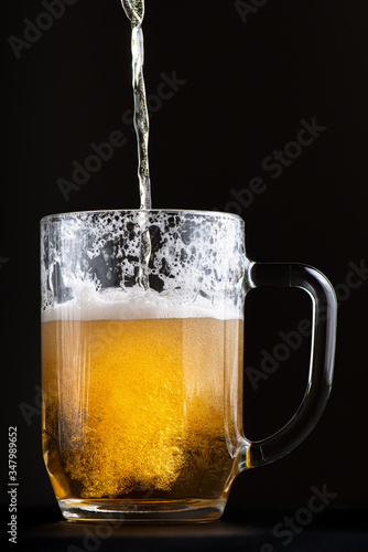 bright and fresh beer is poured into a large glass goblet. Selective focus macro shot with shallow depth of field isolated on black background