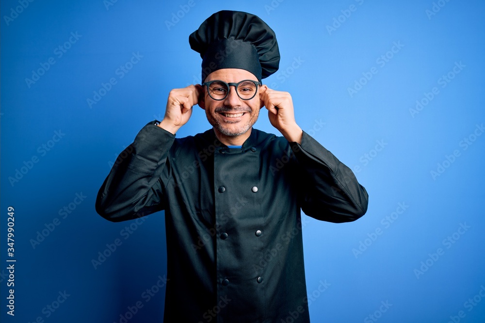 Young handsome chef man wearing cooker uniform and hat over isolated blue background Smiling pulling ears with fingers, funny gesture. Audition problem Young handsome chef man wearing cooker uniform and hat over isolated blue background Smiling pulling ears with fingers, funny gesture. Audition problem