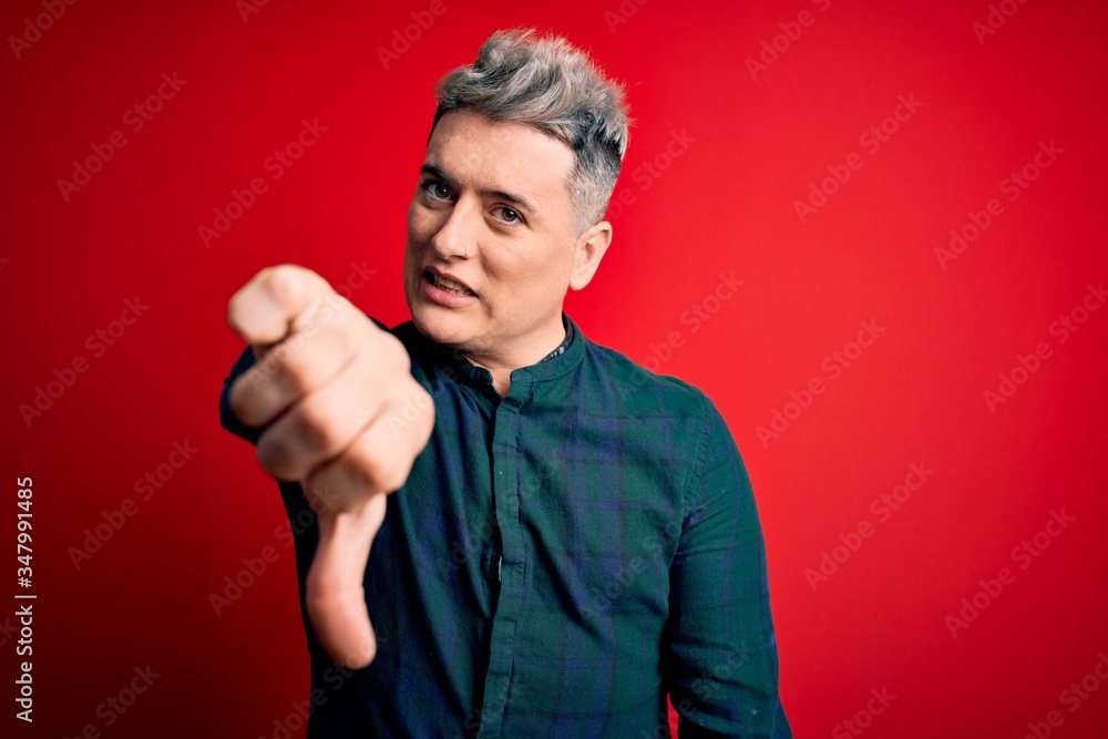 Young handsome modern man wearing elegant green shirt over red isolated background looking unhappy and angry showing rejection and negative with thumbs down gesture. Bad expression. Young handsome modern man wearing elegant green shirt over red isolated background looking unhappy and angry showing rejection and negative with thumbs down gesture. Bad expression.