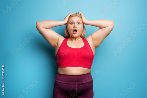 Fat girl is worried because the scale marks a high weight. Cyan background © alphaspirit