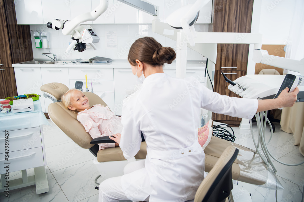 Skillful dentist is examining the teeth of a child. The woman is sitting near the girl trying to set up a contact with her to make her feel comfortable Skillful dentist is examining the teeth of a child. The woman is sitting near the girl trying to set up a contact with her to make her feel comfortable