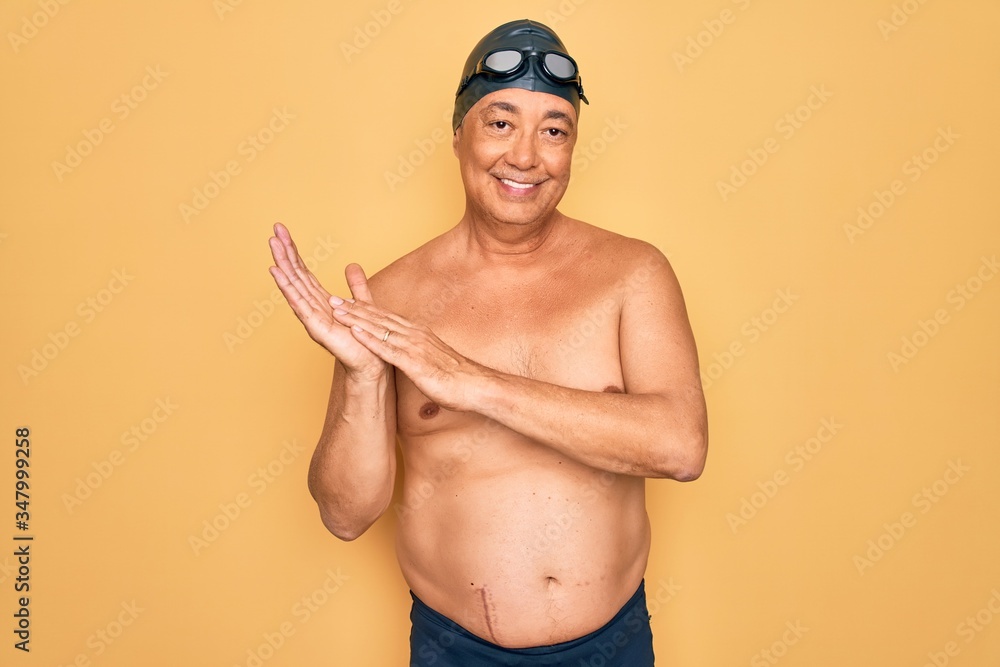 Middle age senior grey-haired swimmer man wearing swimsuit, cap and goggles clapping and applauding happy and joyful, smiling proud hands together