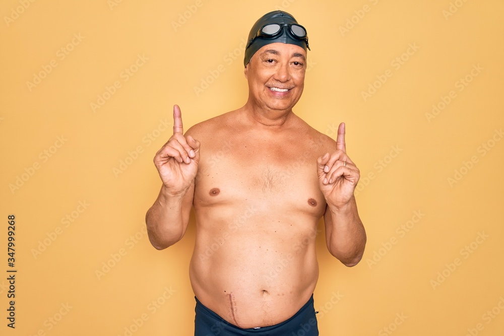 Middle age senior grey-haired swimmer man wearing swimsuit, cap and goggles smiling confident pointing with fingers to different directions. Copy space for advertisement