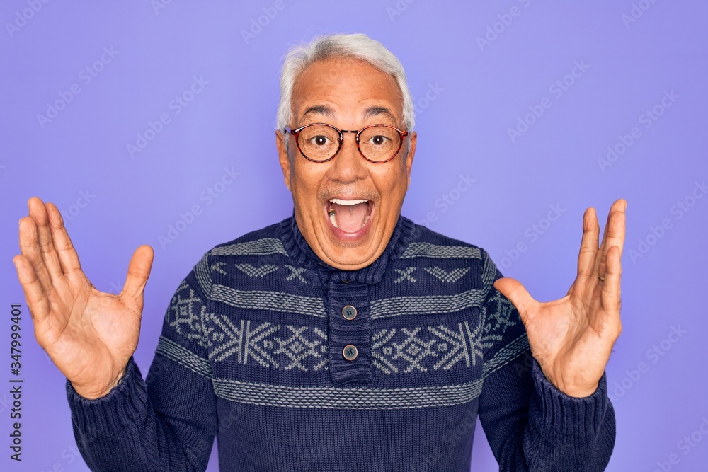 Middle age senior grey-haired man wearing glasses and winter sweater over purple background celebrating crazy and amazed for success with arms raised and open eyes screaming excited. Winner concept Middle age senior grey-haired man wearing glasses and winter sweater over purple background celebrating crazy and amazed for success with arms raised and open eyes screaming excited. Winner concept