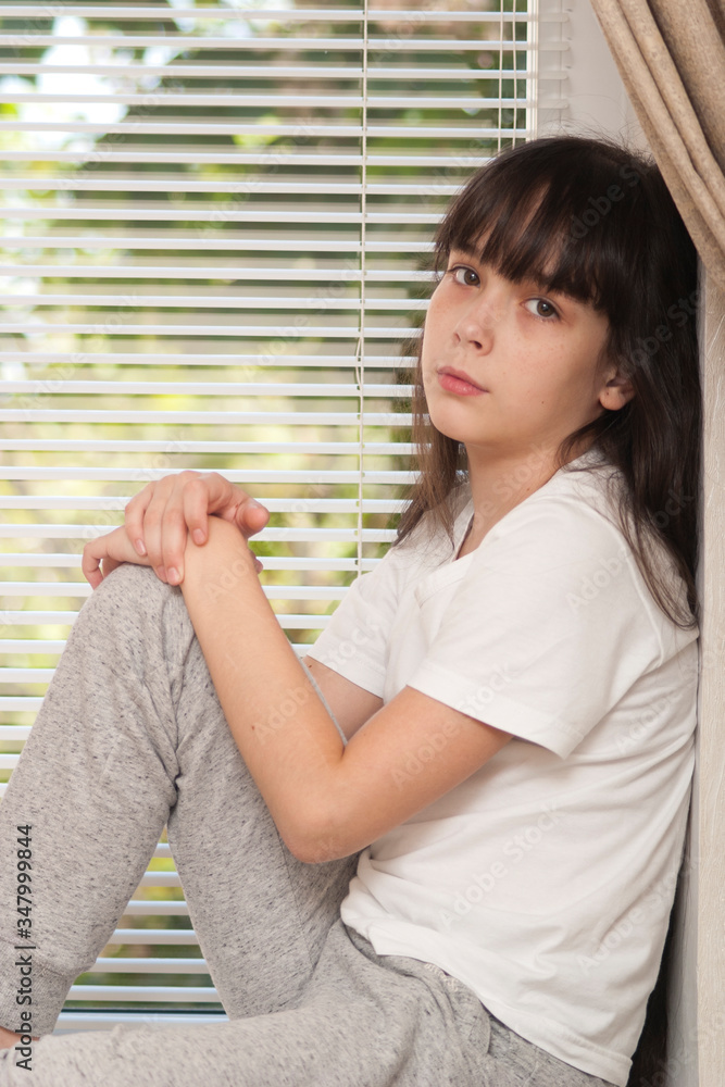 A girl is posing by the window. A girl (ten years old) is sitting on a windowsill by the window. One person A girl is posing by the window. A girl (ten years old) is sitting on a windowsill by the window. One person