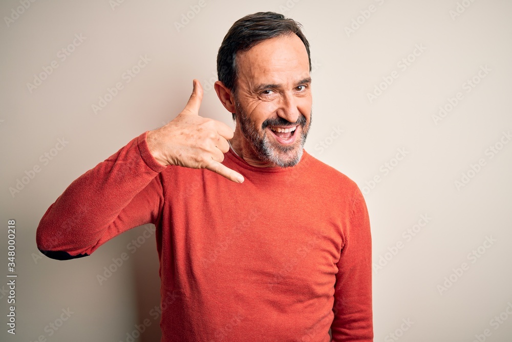 Middle age hoary man wearing casual orange sweater standing over isolated white background smiling doing phone gesture with hand and fingers like talking on the telephone. Communicating concepts. Middle age hoary man wearing casual orange sweater standing over isolated white background smiling doing phone gesture with hand and fingers like talking on the telephone. Communicating concepts.