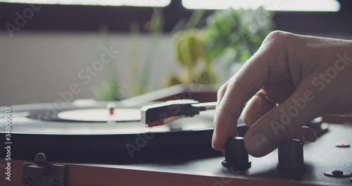 Female hand raising the volume tumbler on vintage portable record player and start paying vynil record