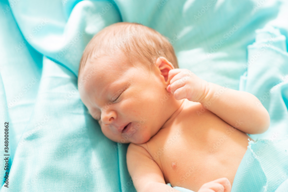 Little caucasian newborn baby falls asleep on blue, delicate and soft blanket. Baby relaxing in safe and calm atmosphere.