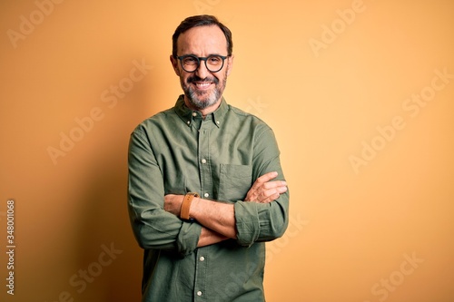 Fotografie Middle age hoary man wearing casual green shirt and glasses over isolated yellow background happy face smiling with crossed arms looking at the camera