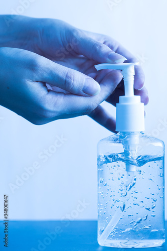 Obraz na płótnie Womans hand using a bottle of hand sanitizer, hand disinfecting gel, crucial for coronavirus prevention through antibacterial hygiene. Pandemic routine, blue medical style w salonie