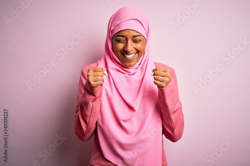 Young African American afro woman wearing muslim hijab over isolated pink background excited for success with arms raised and eyes closed celebrating victory smiling. Winner concept. © Krakenimages.com
