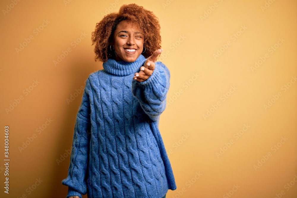 Young beautiful African American afro woman with curly hair wearing blue turtleneck sweater smiling friendly offering handshake as greeting and welcoming. Successful business. Young beautiful African American afro woman with curly hair wearing blue turtleneck sweater smiling friendly offering handshake as greeting and welcoming. Successful business.