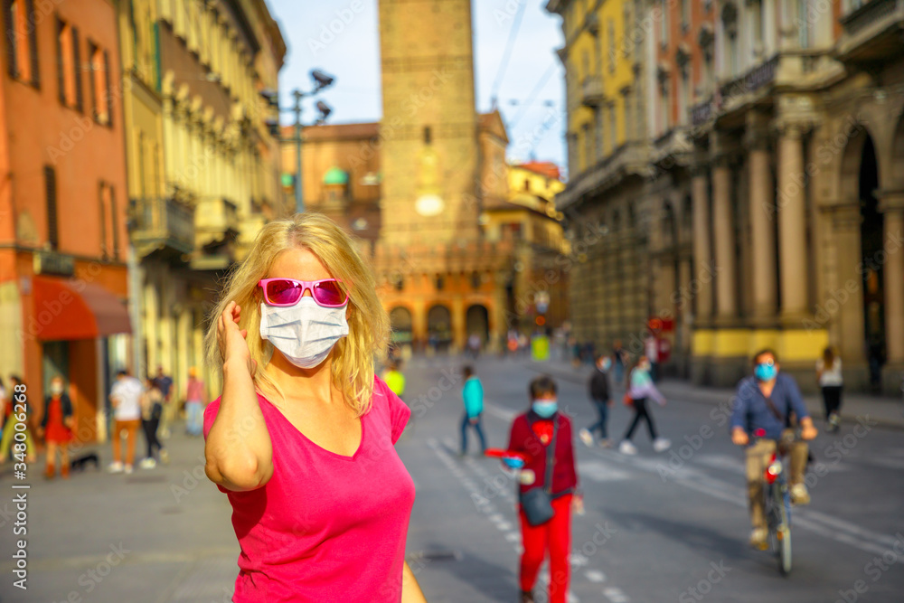 Woman tourist in Italian outbreak with a surgical mask and sunglasses. Two Towers building in Bologna town. COVID-19 Coronavirus quarantine prevention in Italy.