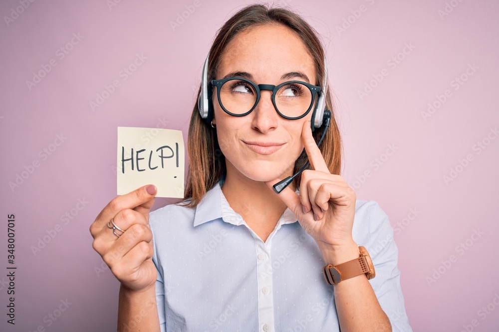 Beautiful call center agent woman working using headset holding help reminder message serious face thinking about question, very confused idea Beautiful call center agent woman working using headset holding help reminder message serious face thinking about question, very confused idea
