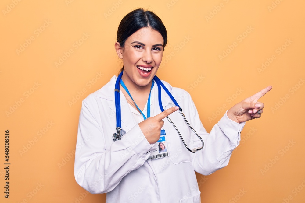 Young beautiful doctor woman wearing stethoscope and id card over isolated yellow background smiling and looking at the camera pointing with two hands and fingers to the side. Young beautiful doctor woman wearing stethoscope and id card over isolated yellow background smiling and looking at the camera pointing with two hands and fingers to the side.