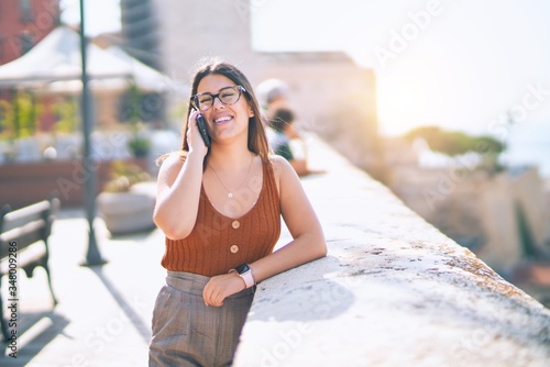 Young beautiful woman smiling happy and confident. Standing with smile on face talking by the smartphone at the city © Krakenimages.com
