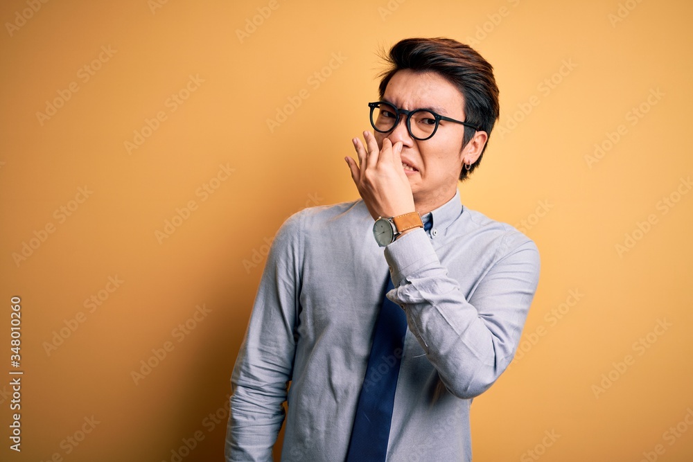 Young handsome chinese businessman wearing glasses and tie over yellow