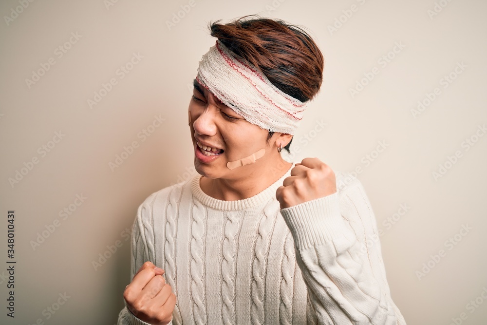 Young handsome chinese man injured for accident wearing bandage and strips on head celebrating surprised and amazed for success with arms raised and eyes closed. Winner concept. Young handsome chinese man injured for accident wearing bandage and strips on head celebrating surprised and amazed for success with arms raised and eyes closed. Winner concept.