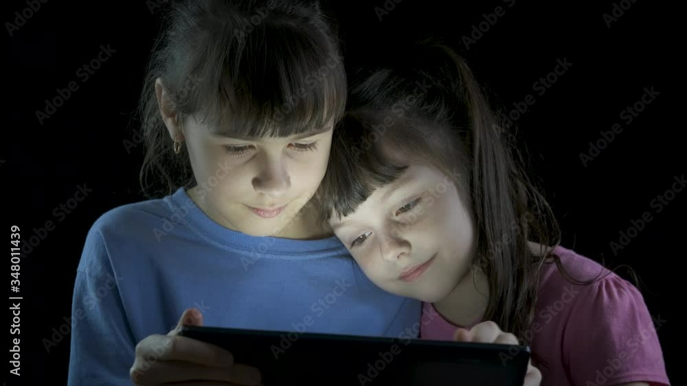 Children watch a video on a gadget. Cute little girls surfing the internet at night on a tablet. The concept of child dependence on the Internet. Children watch a video on a gadget. Cute little girls surfing the internet at night on a tablet. The concept of child dependence on the Internet.