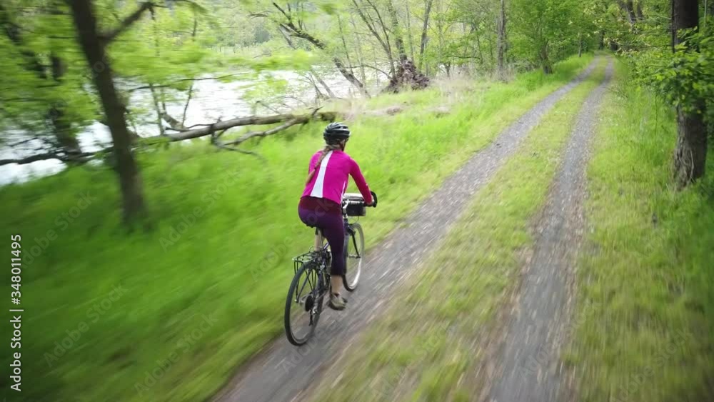 High angle camera flying above a woman mountain biking on a path in a forest. High angle camera flying above a woman mountain biking on a path in a forest.