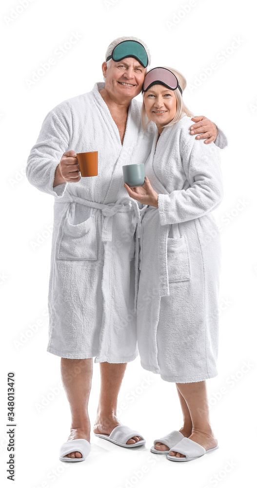 Mature couple in bathrobes and with sleep masks drinking tea on white background Mature couple in bathrobes and with sleep masks drinking tea on white background