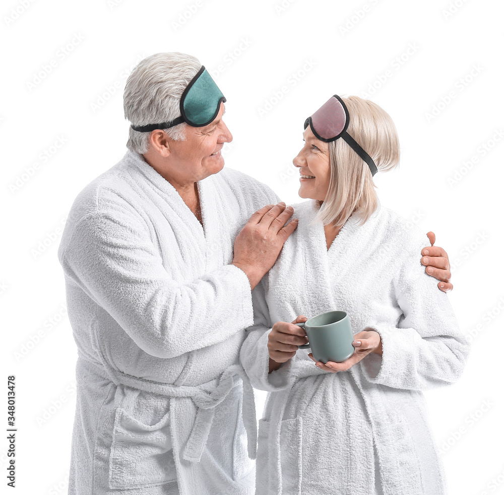 Mature couple in bathrobes and with sleep masks on white background