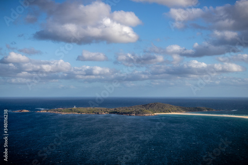 view of the sea with an island and a light house at the top connected to main land by a sandbank and clouds in the sky