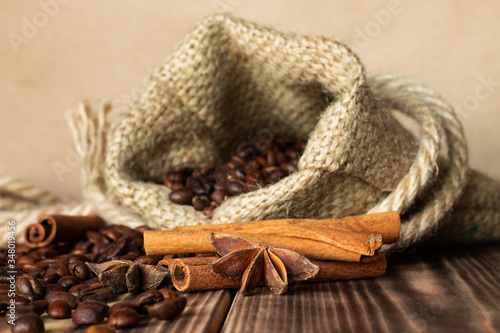 Coarse burlap sack with sprinkled grains of coffee on a burnt wood tabletop with cinnamon sticks and anise stars. Copy space. photo