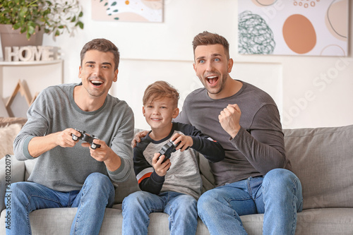 Happy gay couple with adopted child playing video game at home