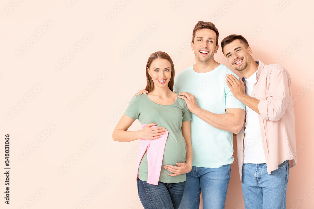 Gay couple and pregnant woman with baby clothes on color background Gay couple and pregnant woman with baby clothes on color background