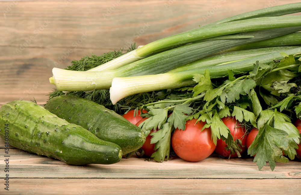 Green onions, parsley, dill, tomatoes and cucumbers on a wooden table.