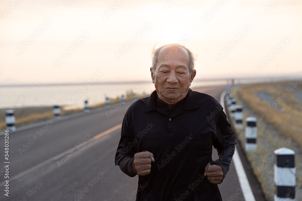 Front view Asian elderly exercise happy smile. Close up Senior man running on road in the morning sunshine. health lifestyle and exercise Concept. Front view Asian elderly exercise happy smile. Close up Senior man running on road in the morning sunshine. health lifestyle and exercise Concept.