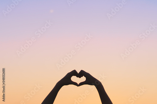 Woman hand do heart shape on blue sky and bokeh background.