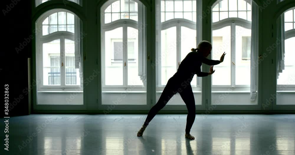 black female silhouette on a background of arched Windows. the woman spreads her legs and slowly bends to the floor black female silhouette on a background of arched Windows. the woman spreads her legs and slowly bends to the floor