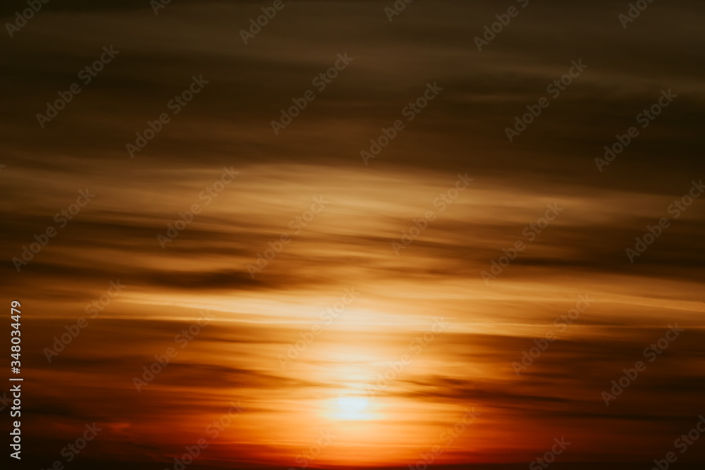 Abstract fantastic background. Bright orange and yellow sky with sunbeams and dark clouds. Apocalyptic sunrise or sunset