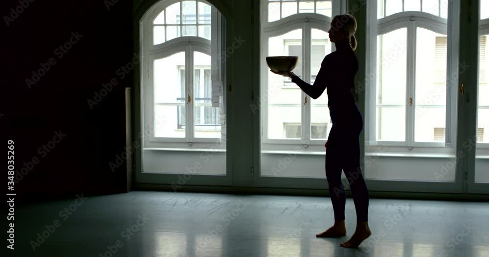 black female silhouette on a background of arched Windows. the woman holds a singing bowl and stick and swings black female silhouette on a background of arched Windows. the woman holds a singing bowl and stick and swings