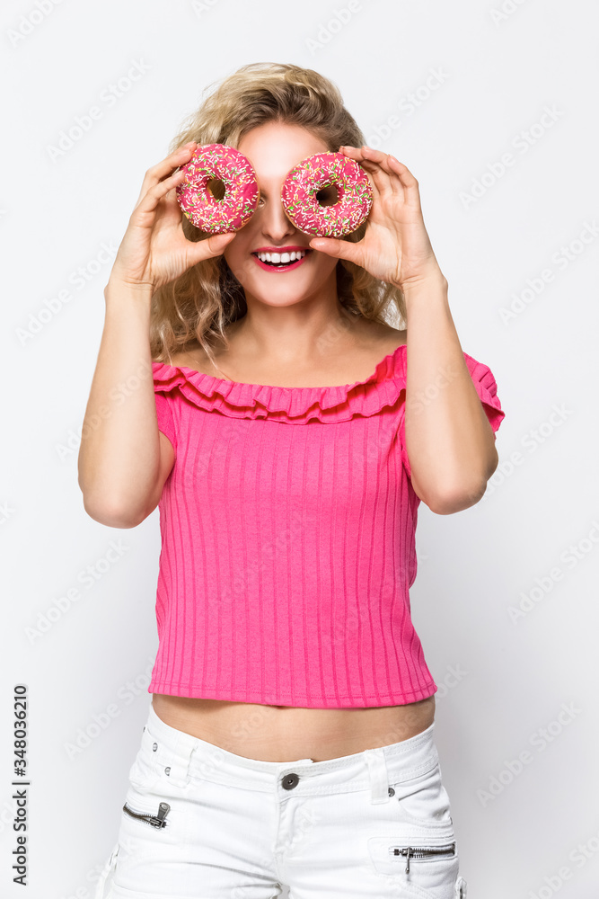 Food Ideas. Portrait of Cute and Funny Caucasian Blond Girl Enjoying Pink Doughnut in Hands. Posing in Sexy Shorts Against White. Food Ideas. Portrait of Cute and Funny Caucasian Blond Girl Enjoying Pink Doughnut in Hands. Posing in Sexy Shorts Against White.