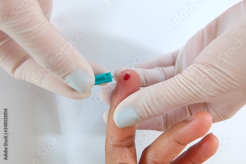 Close up hand wearing white gloves of a nurse or doctor or technician holding needle punch finger patient blood sample storage at fingertips to determine blood with small drop of blood.