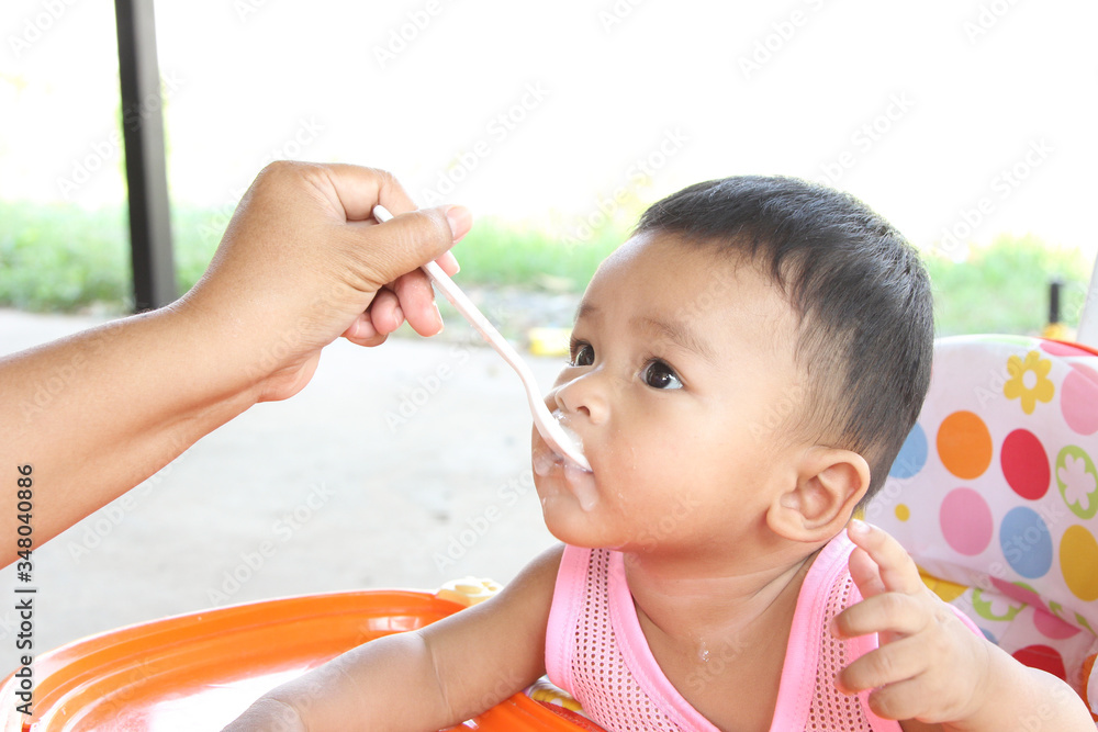 Asian boy 6 months old eating rice porridge and porridge dirty her mouth. Mother feed the son.
