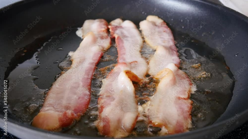 Bacon sizzling in a frying pan. Delicious, unhealthy breakfast meat fries in a skillet. Pork products are experiencing a supply chain issue and shortages due to the Coronavirus pandemic. Bacon sizzling in a frying pan. Delicious, unhealthy breakfast meat fries in a skillet. Pork products are experiencing a supply chain issue and shortages due to the Coronavirus pandemic.