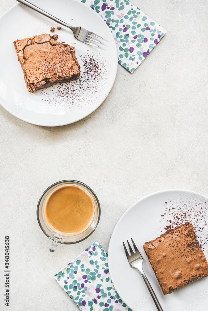 Top view of a cup of coffee and two dessert plates with brownie cake over white rustic background.