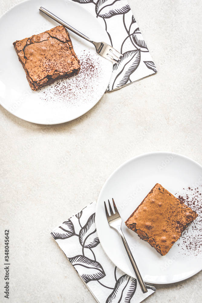 Top view of two dessert plates with brownie cake over white rustic background.
