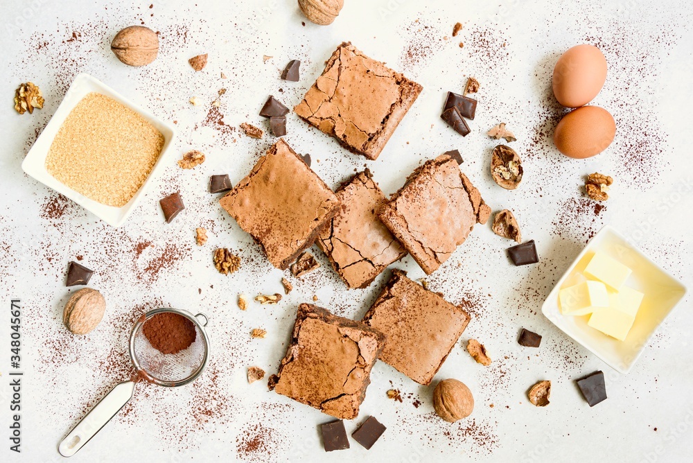 Top view of freshly baked home made brownie cake arranged with recipe ingredients over white rustic background.