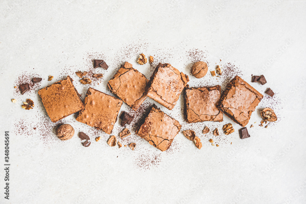 Top view of freshly baked home made brownie cake arranged with nuts, chocolate and cocoa powder over white rustic background.