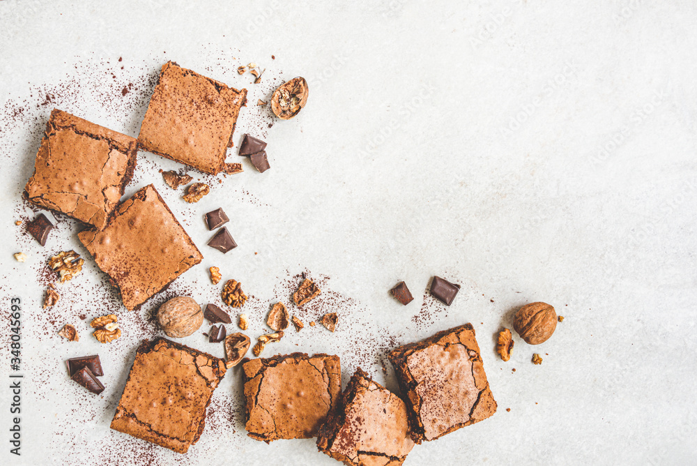 Top view of freshly baked home made brownie cake arranged with nuts, chocolate and cocoa powder over white rustic background.