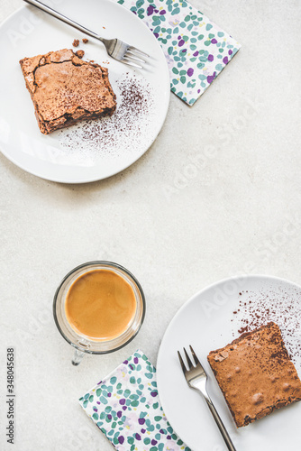 Obraz na płótnie Top view of a cup of coffee and two dessert plates with brownie cake over white rustic background. w salonie