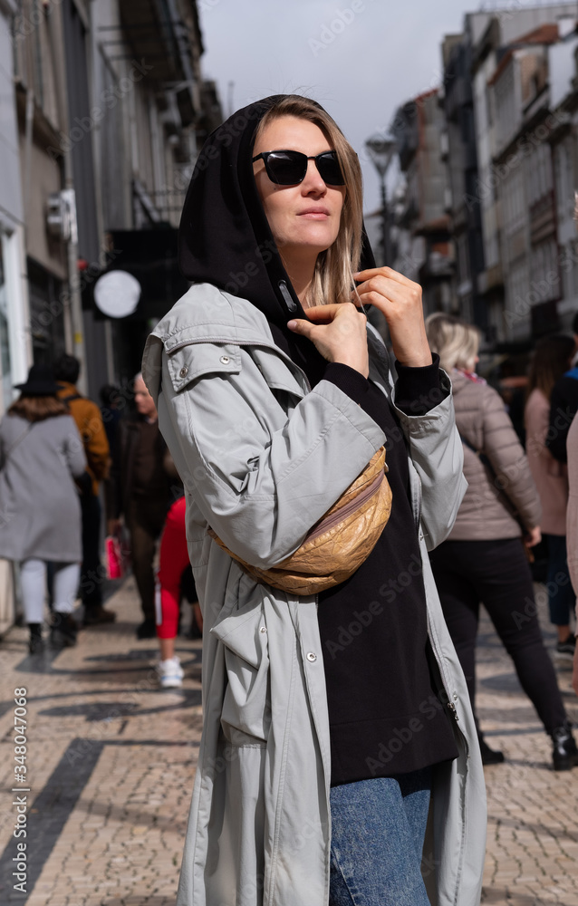 A stylish woman in a trench coat stands on a busy street