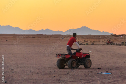 Young man in safari trip through egyptian desert driving ATV at sunset. Quad bikes safari in the desert near Hurghada, Egypt