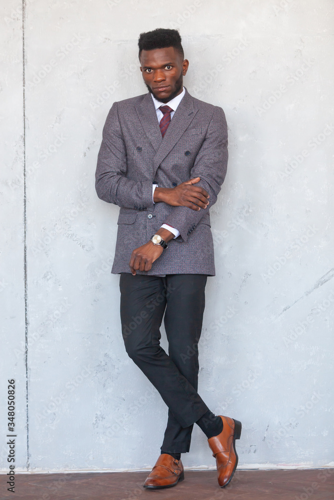 Full length portrait of confident handsome african business man posing in modern grey suit against a gray concrete wall Full length portrait of confident handsome african business man posing in modern grey suit against a gray concrete wall